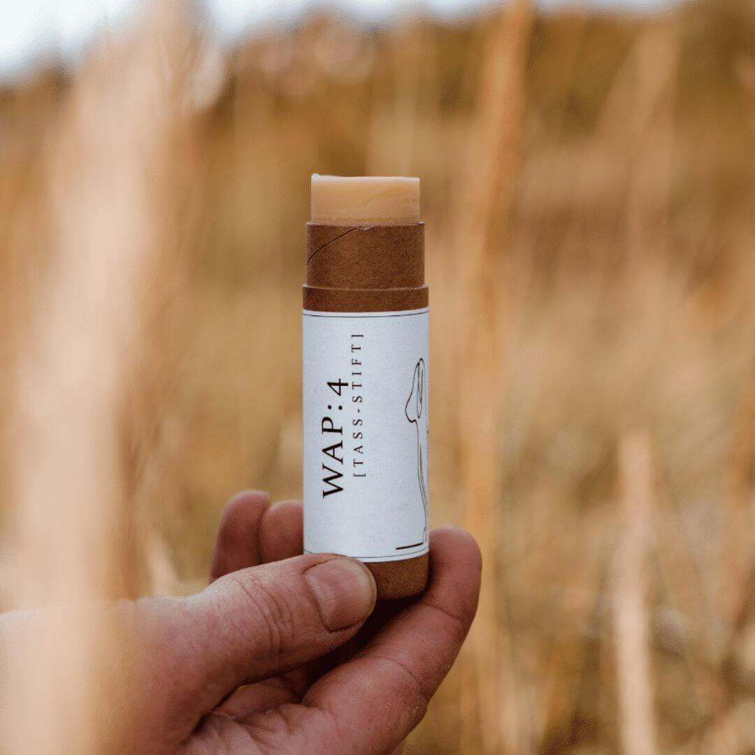 Tassuvoidepuikko pahvisessa pakkauksessa miehen kädessä heinikossa.